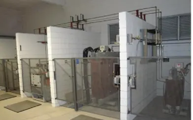 Cubículos da subestação de média tensão, separados por paredes de azulejo branco e grades de proteção, com transformador e chaves ao fundo.