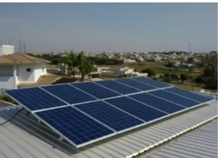 Módulos fotovoltaicos instalados sobre telhado metálico, com casas do condomínio e a cidade ao fundo.